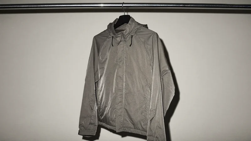 Wasserabweisende Laufjacke an einer schlichten Stahlstange vor heller Wand